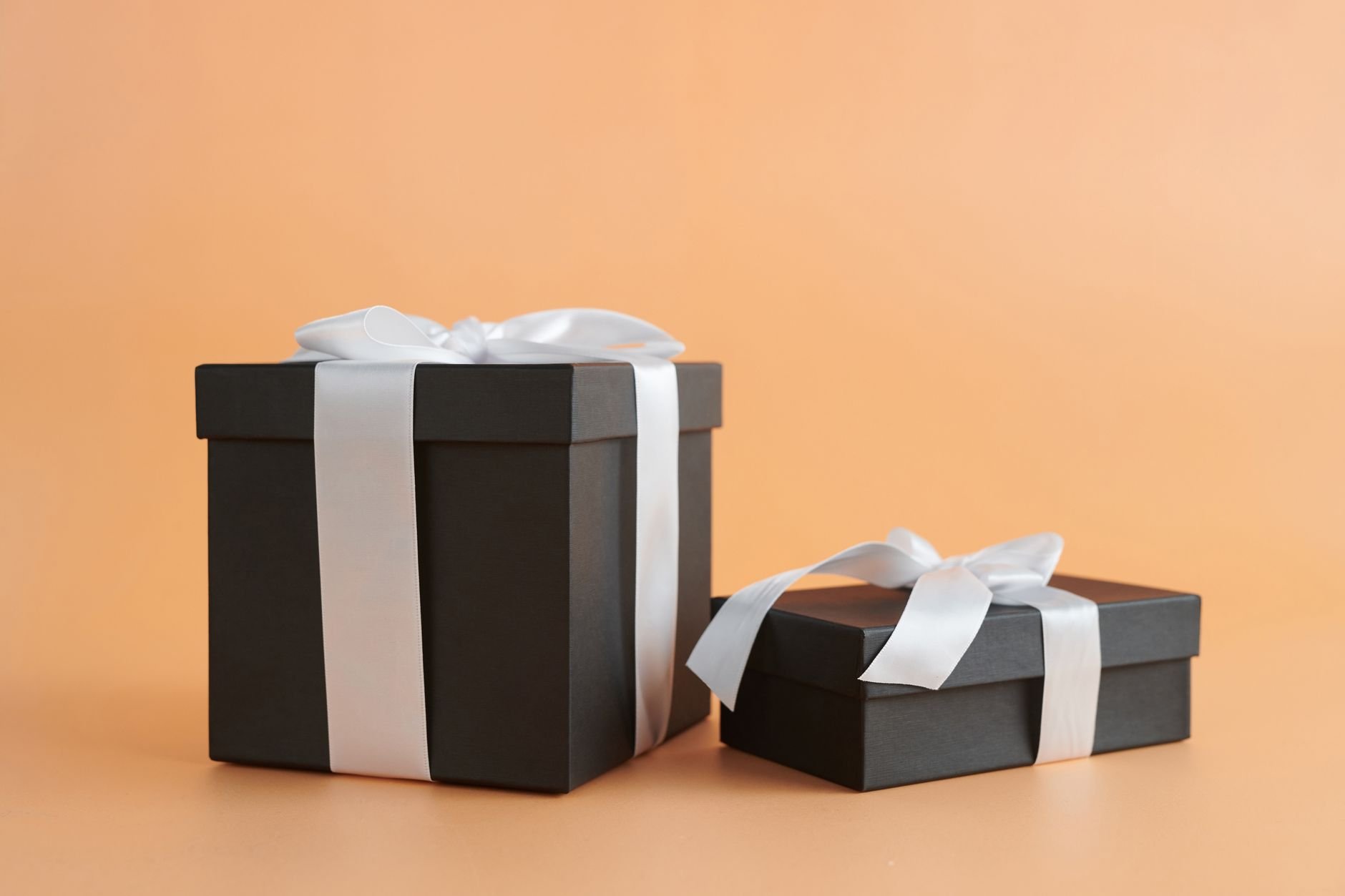 Two black gift boxes with white ribbons on a beige background